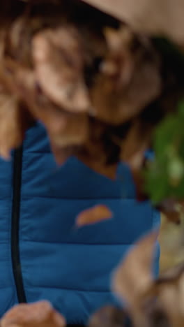 primer plano de una persona con suéter azul volviendo la bolsa marrón al revés, soltando hojas secas en el suelo en un entorno al aire libre rodeado de follaje de otoño y entorno natural