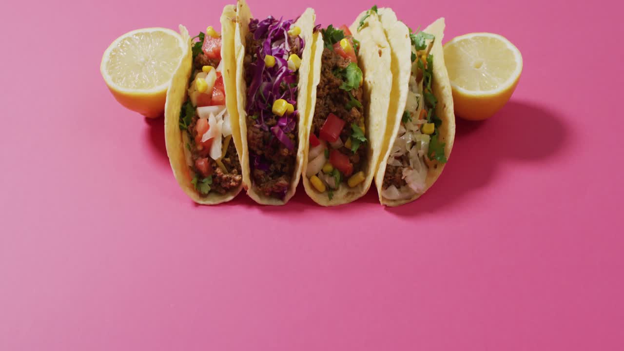 Video af frisk tilberedte tacos liggende på et bræt på lyserød baggrund.