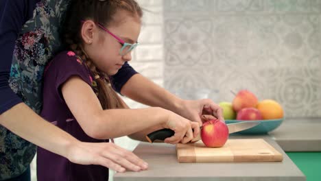 Mutter-Hilft-Tochter,-Apfel-Auf-Schneidebrett-Zu-Schneiden.-Mutter-Kocht-Mit-Kind-In-Der-Hand