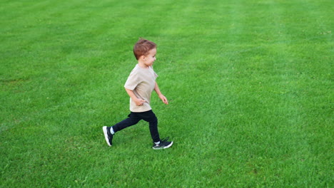 cute caucasian baby boy runs joyfully by the green grass. energetic toddler kid plays with a ball outdoors.