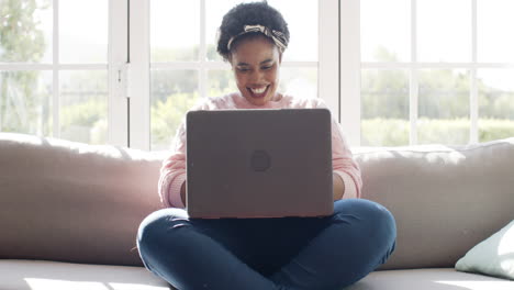 mujer afroamericana sonríe usando una computadora portátil en un sofá en casa