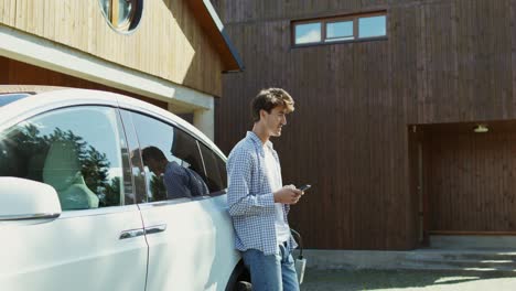 man using phone next to an electric car at home