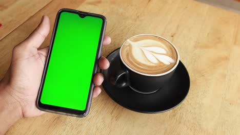Sosteniendo-Una-CPU-De-Café-Y-Usando-Un-Teléfono-Inteligente-Con-Pantalla-Verde