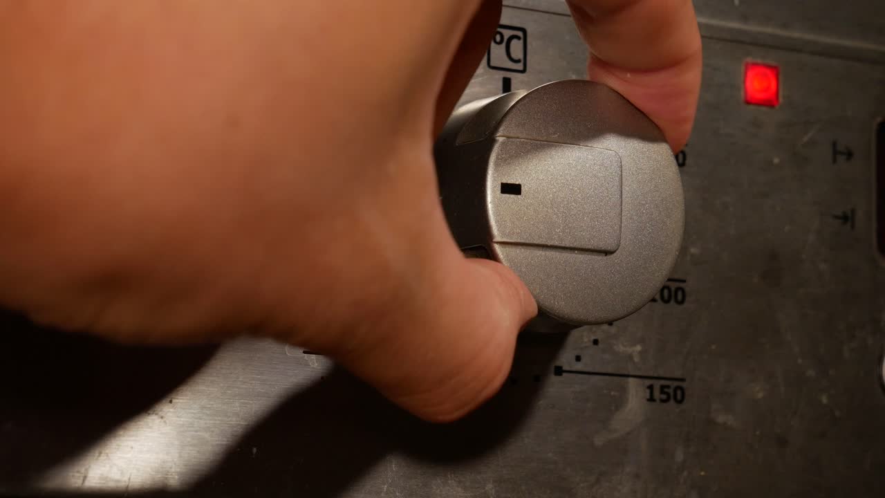 primer plano de la mano humana que regula el modo de cocción en el panel del horno en la cocina