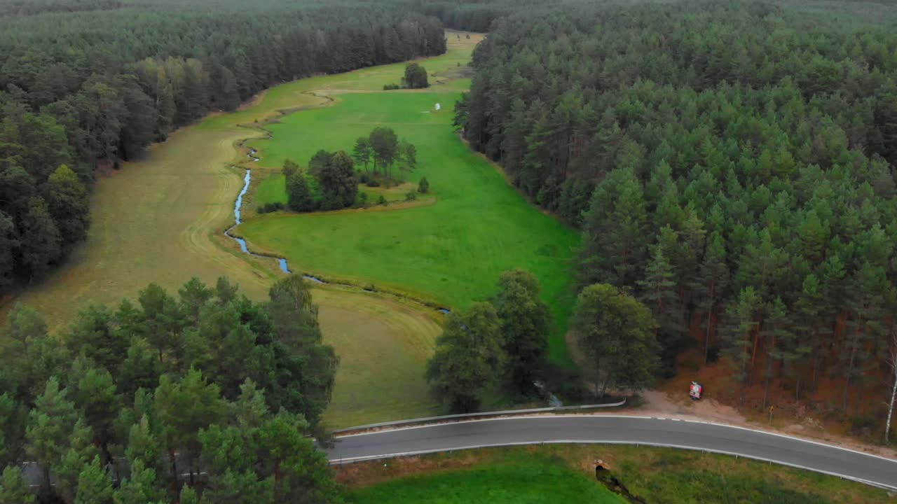 Aerial shot of an empty road between trees going across glacial valley and small creek in wdzydze kiszewskie, poland.