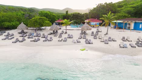 aerial trucking pan along white sandy beach and turquoise waters at grote knip or playa abou, curacao, surrounded by lush greenery and clear blue skies