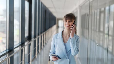 Medium-plan-portrait-of-a-young-girl-in-a-blue-suit-with-a-passport-and-a-phone-walking-down-a-glass-corridor