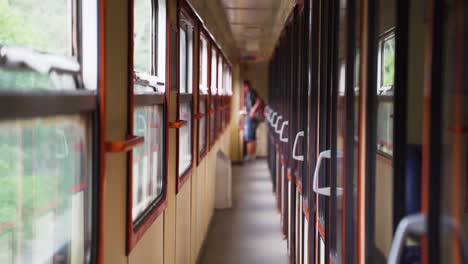 a passenger with backpack looking out the window of a train's corridor.