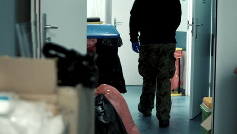 a man dressed in military trousers is walking through a hospital corridor, the waste is placed in bags