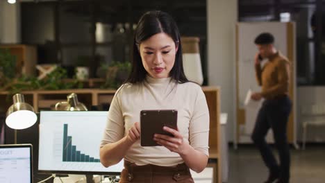 Video-of-happy-asian-woman-with-tablet-working-late-in-office