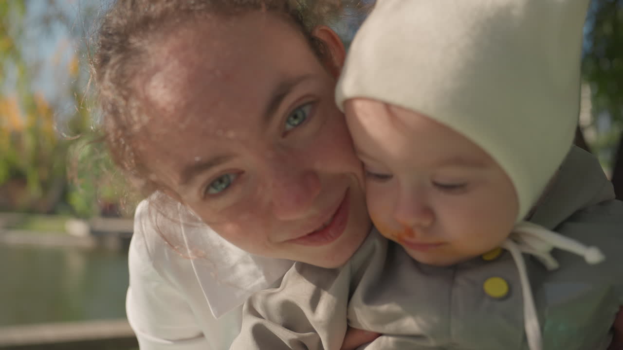 Abbraccio di calore familiare. Serenità all'aperto di madre e neonato. Momento pacifico della madre che tiene in braccio il bambino vicino a un'acqua tranquilla. Legame emotivo tra madre e figlio in un tranquillo scenario lacustre con la natura