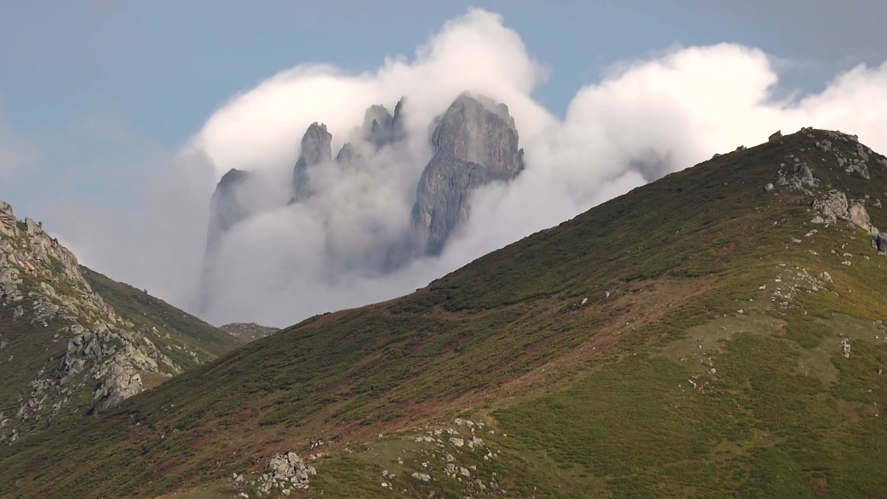 Nuvole in movimento sopra cime montuose frastagliate in un paesaggio verde