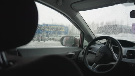 car interior captured during winter with water droplets on glass and soft urban blur through window, side mirror reflecting person approaching and opening back door outside in snowy environment