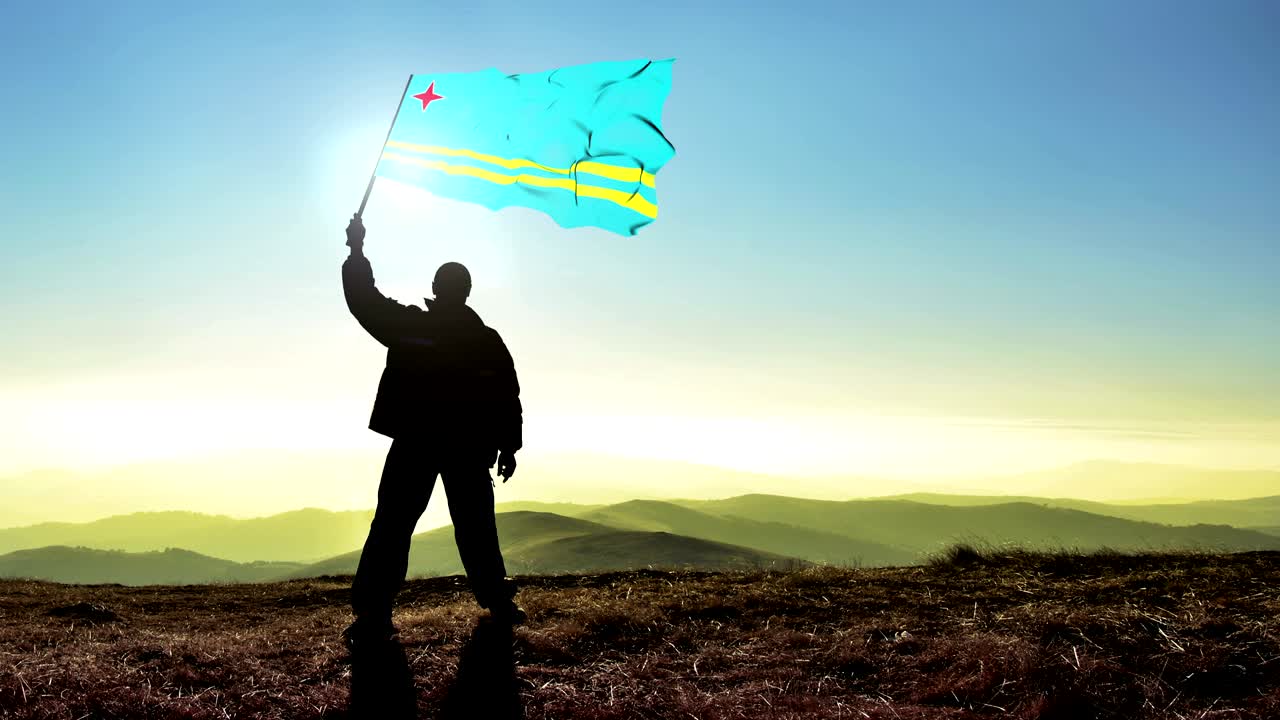 Silueta de hombre exitoso ganador ondeando la bandera de Aruba en la cima de la montaña. Fondo de cinemagraph en bucle.