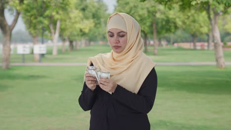 serious muslim woman counting money in park