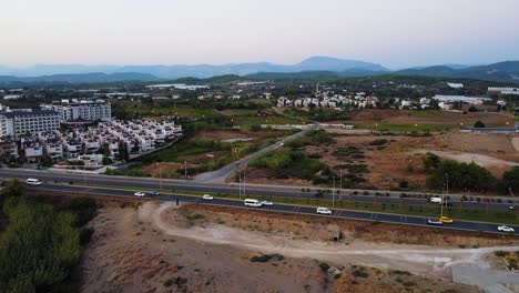 Luftaufnahmen-Von-Autos,-Die-Von-Der-Stadtautobahn-In-Der-Wüste-Mit-Bergsilhouetten-Fahren