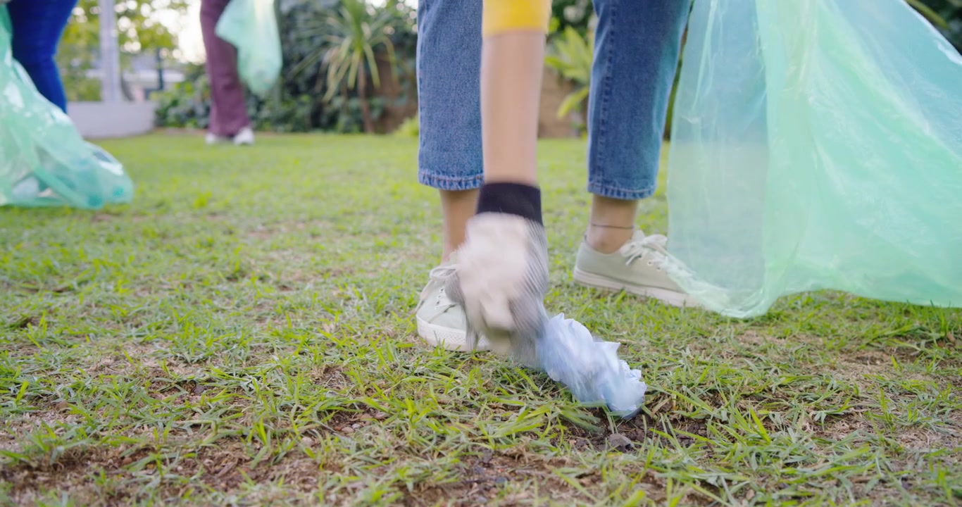 3 women volunteers approaching litter on lawn picking bottle paper cup into green bag for cleanup