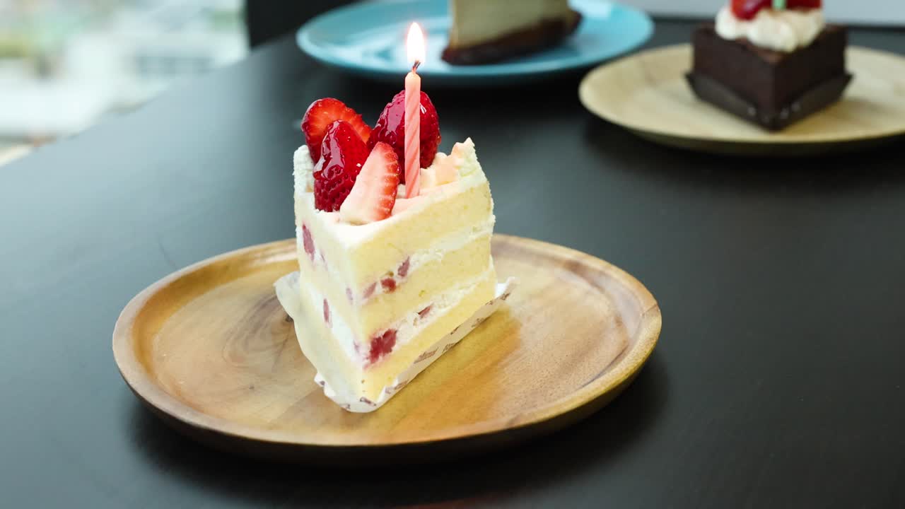 Strawberry shortcake slice with lit candle on wooden plate, bright natural lighting, static shot