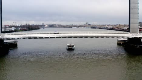 Jacques-Chaban-Delmas-Bridge-in-Bordeaux-France-with-car-traffic-and-a-boat-passing-below-it-on-the-Garonne-river,-Aerial-dolly-out-reveal-shot