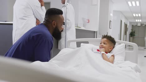 african american male doctor talking to child patient laying in bed at hospital