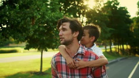Father-giving-son-piggyback-riding-in-park.-Man-and-boy-talking-on-street