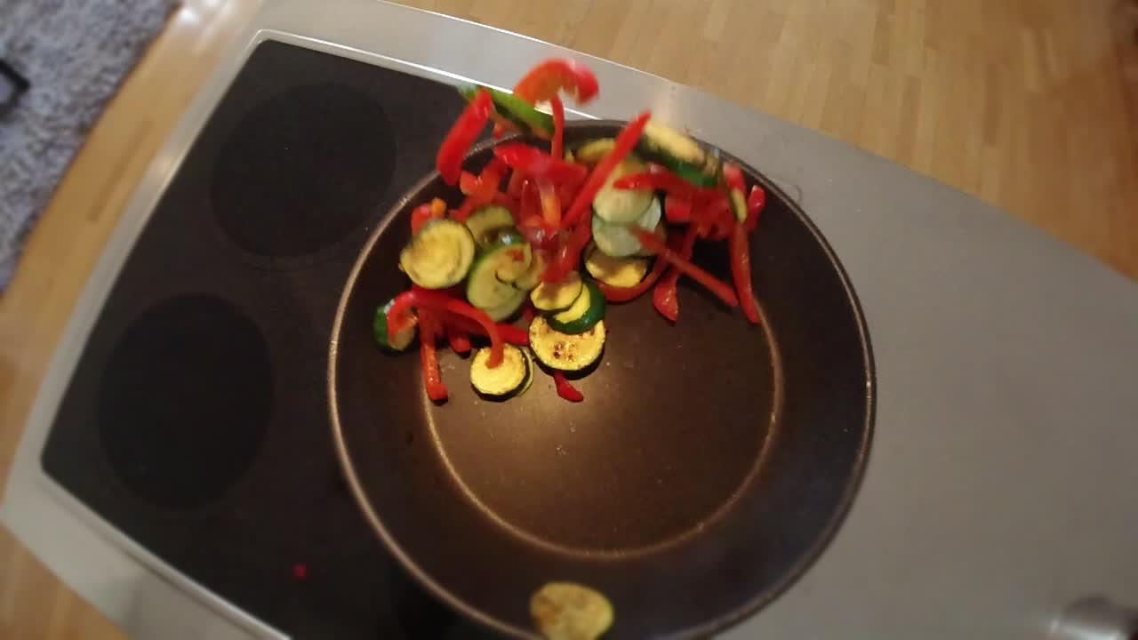 A chef stirring vegetables in a frying pan in a non-commercial kitchen. From a top down perspective in slow motion.