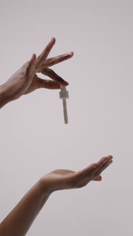 close up of woman squeezing dropper from bottle of beauty product on white background