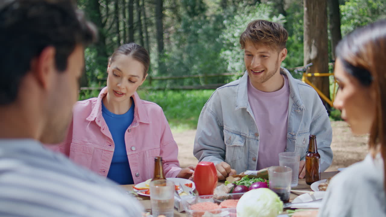 Picnic friends talking forest sitting at wooden table with food drinks closeup