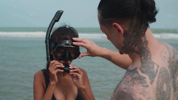 Man helping woman to wear diving goggles