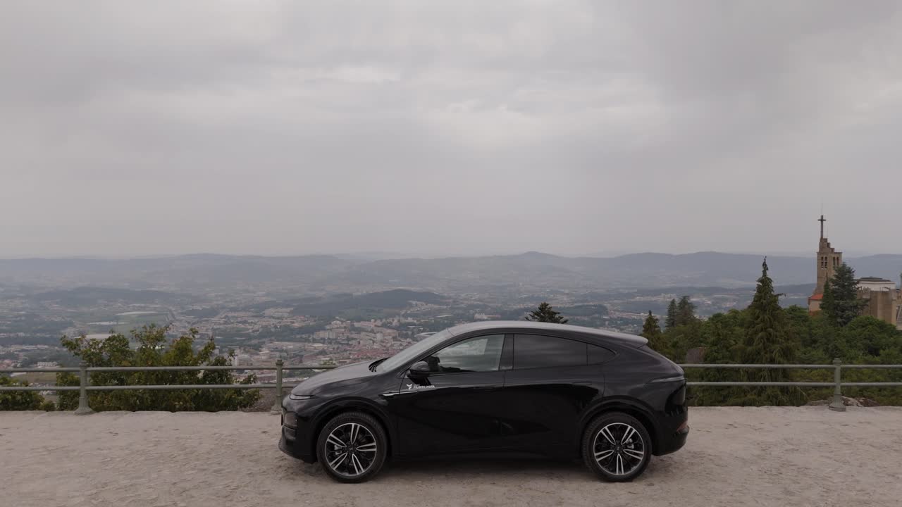 Auto nera parcheggiata in un belvedere collinare con un ampio paesaggio vallivo sullo sfondo.