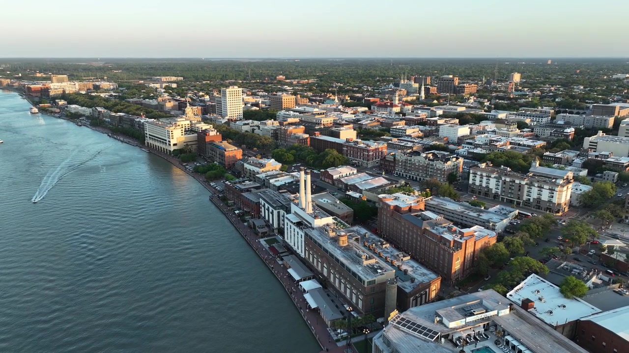 Veduta aerea con drone del centro di Savannah, Georgia, al tramonto, che mostra lo storico lungofiume, il Municipio con cupola dorata e il caldo bagliore del sole che tramonta sulla città.