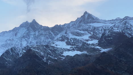 Swiss-alps-autumn-first-snow-dusting-mountain-peaks-Saas-Fee-Zermatt-Saastal-alpine-valley-chalet-ski-resort-town-sunset-yellow-pink-high-clouds-Switzerland-Europe-cinematic-pan-up-reveal