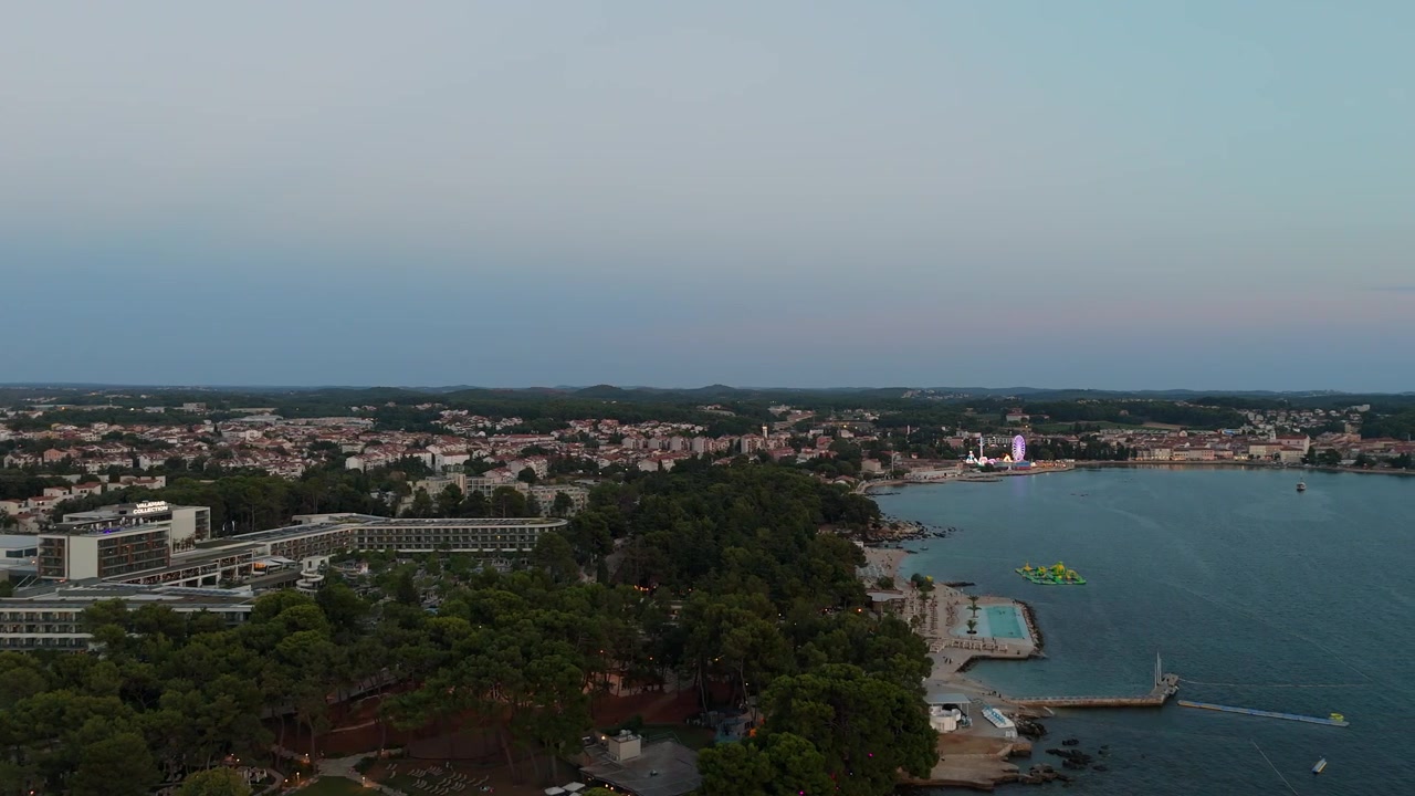 Parenzo Croazia al tramonto, vista aerea con drone della splendida città vecchia, hotel costieri, spiagge soleggiate, lungomare, ruota panoramica e giostre durante una calda serata estiva sulla costa adriatica