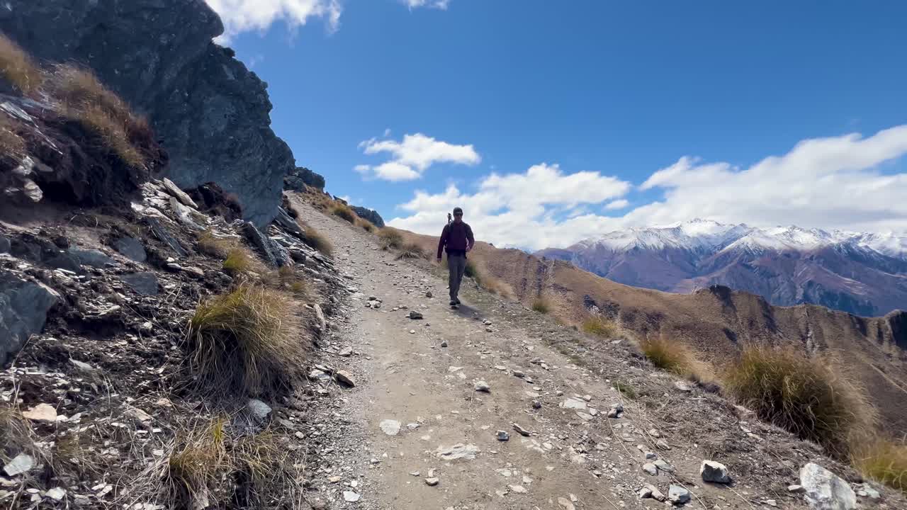 Hiker on a scenic mountain trail with snowy peaks, feeling adventurous and free