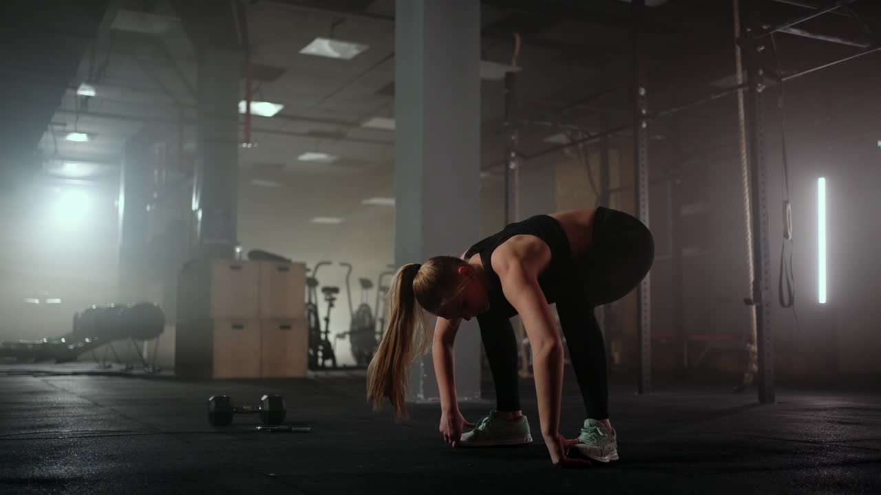 Una donna esegue esercizi di stretching in una sala fitness buia dopo un allenamento. Donna fitness che si allena sui muscoli del core in una palestra buia.