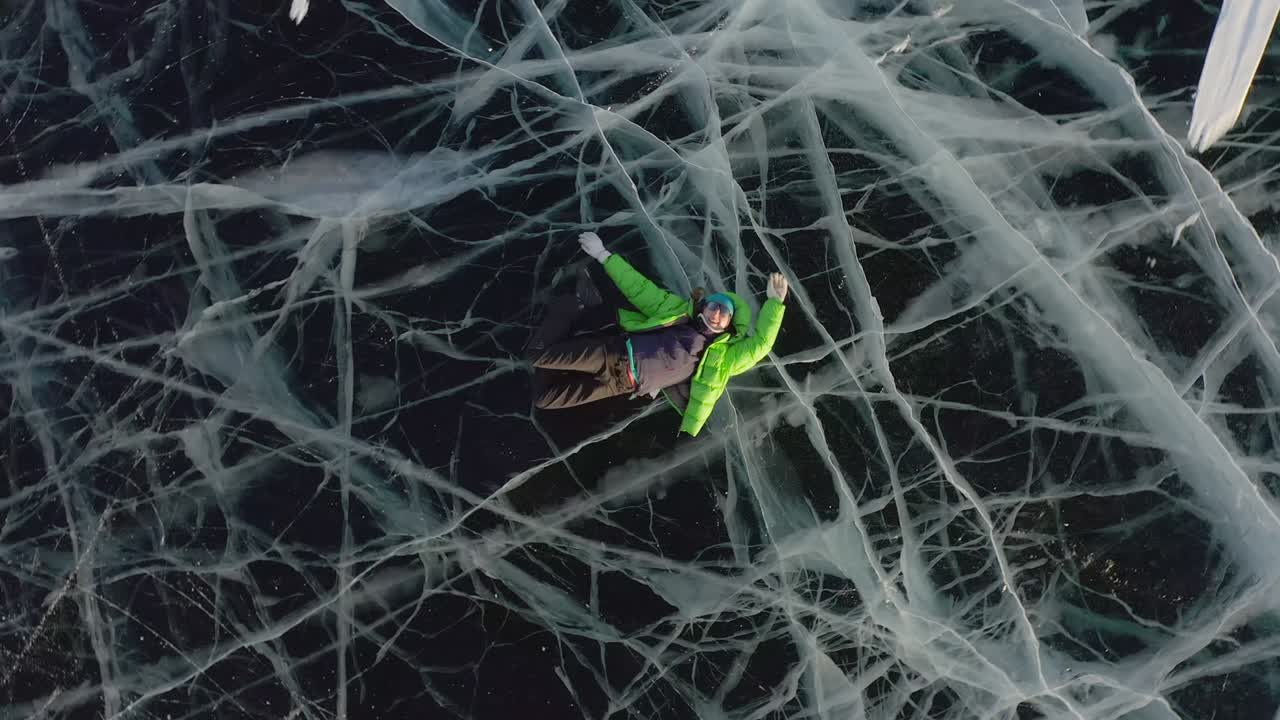 una niña yace en el hielo en invierno, agitando sus brazos y piernas hacia el lado, representando a un ángel