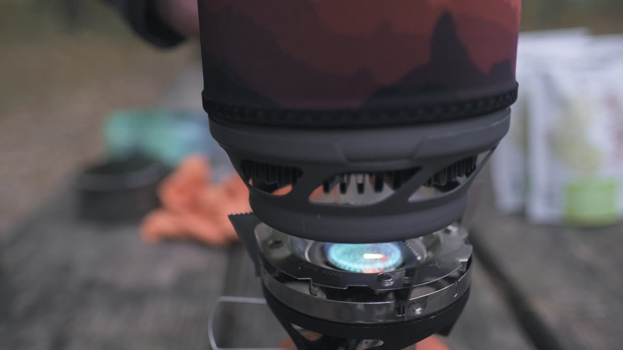 남자는 단일 버너 가스 캠핑 스토브에 작은 요리 냄비를 놓습니다.