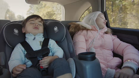 los niños que duermen conducen en el asiento trasero del coche. un bebé asiático duerme en un asiento para niños, una chica duerme a su lado.