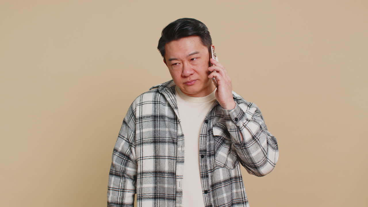 Disinterested tired asian man having annoyed boring talk on smartphone online conversation quarrel