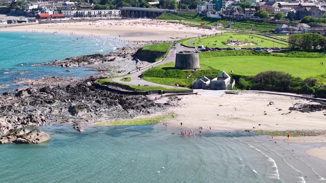 Gente saltando al mar desde una playa de arena en Balbriggan, día soleado de verano en Irlanda