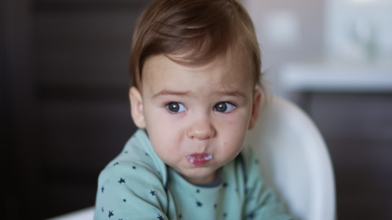 Giving food to a little toddler. Mom's hand shoving the spoon with food to a baby's mouth. Close up. Blurred backdrop.