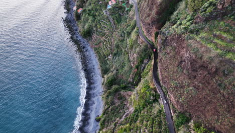 cars drive scary cliffside road under cascading anjos waterfall, madeira