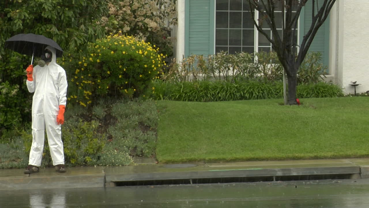 un hombre con traje de materiales peligrosos sostiene un paraguas y cruza la calle