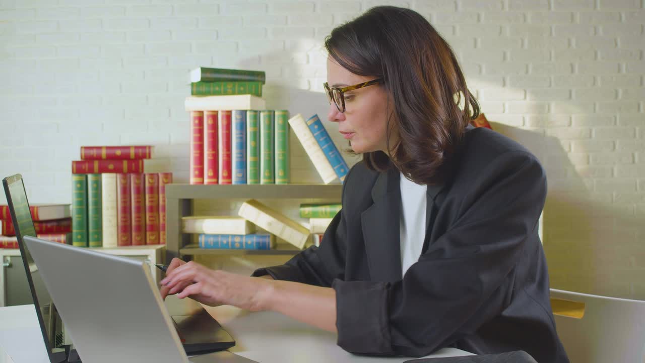 mujer de negocios de mediana edad se pone gafas y comienza a trabajar en una computadora en la oficina