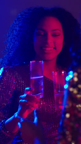 vertical video of two women dancing in nightclub or bar celebrating doing cheers and drinking alcohol with sparkling lights