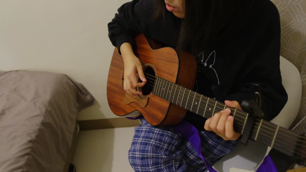 mujer caucásica en pijama y capucha negra tocando guitarra acústica