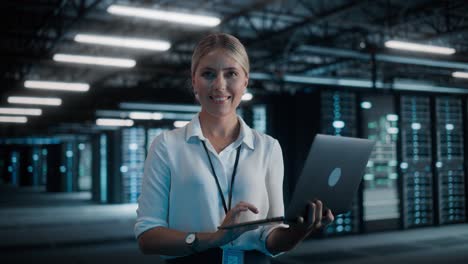 retrato de una mujer exitosa directora de tecnología usando una computadora portátil, de pie en un gran centro de datos de almacén, mirando a la cámara. administrador de sistemas mantenimiento de saas, servidor de servicios en la nube