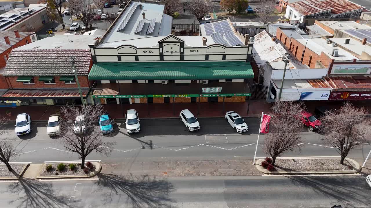 Drone footage captures parked cars, moving vehicles, and commercial buildings on a sunny day in Coonabarabran, New South Wales, with steady overhead movement