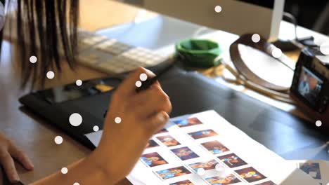 animation of white dots floating over hands of mixed race woman working with photos