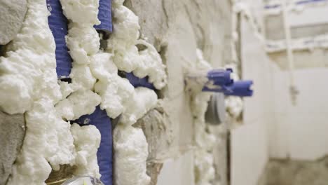 an extreme close up shot of blue water pipes covered in white expanding insulation foam embedded into a bathroom wall, the pipes and drainage system have been upgraded during a refurbishment project